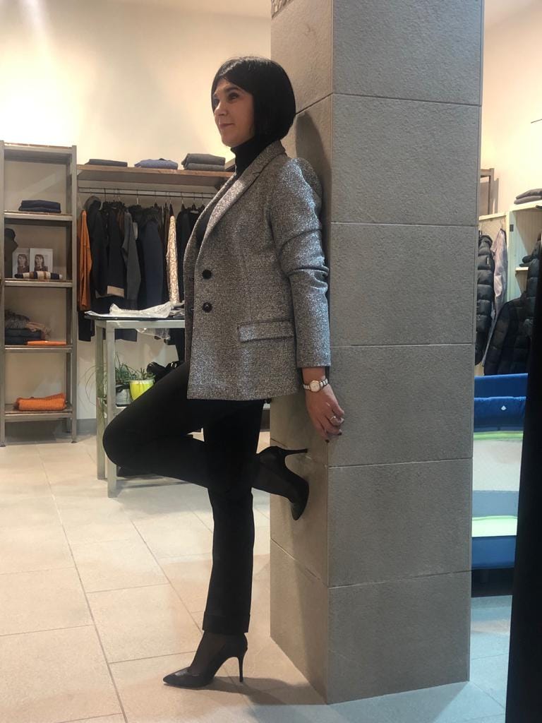 Silvia che indossa un blazer grigio e posa davanti a uno specchio in un negozio di abbigliamento